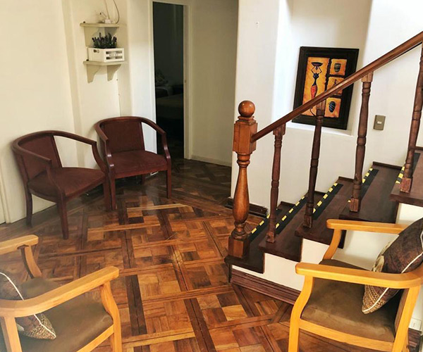 Interior de Residencia Los Andes con escalera de madera y sillones de espera